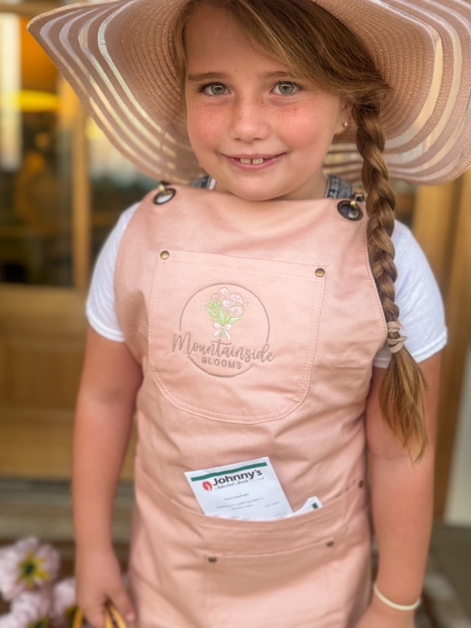 Our daughter wearing a sun hat and a pink Mountain Side Blooms apron with seed packets in the pocket